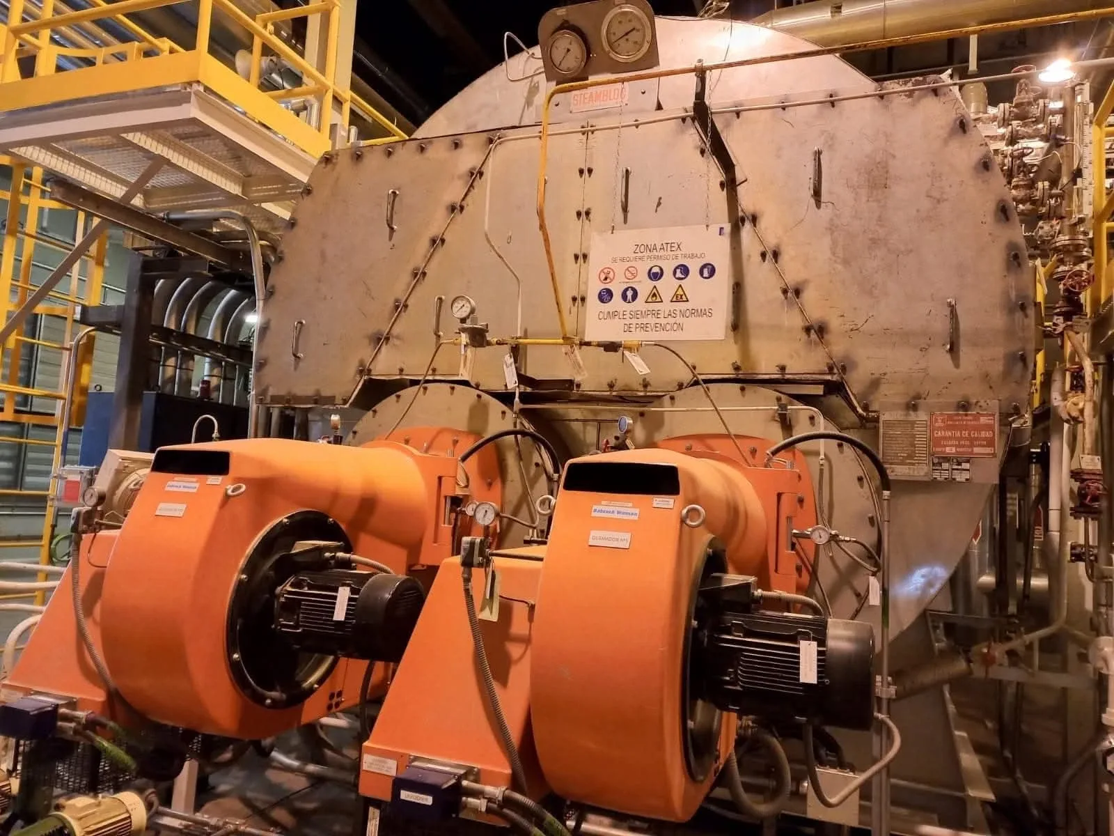 Caldera de vapor industrial con dos quemadores naranjas en una sala de calderas
