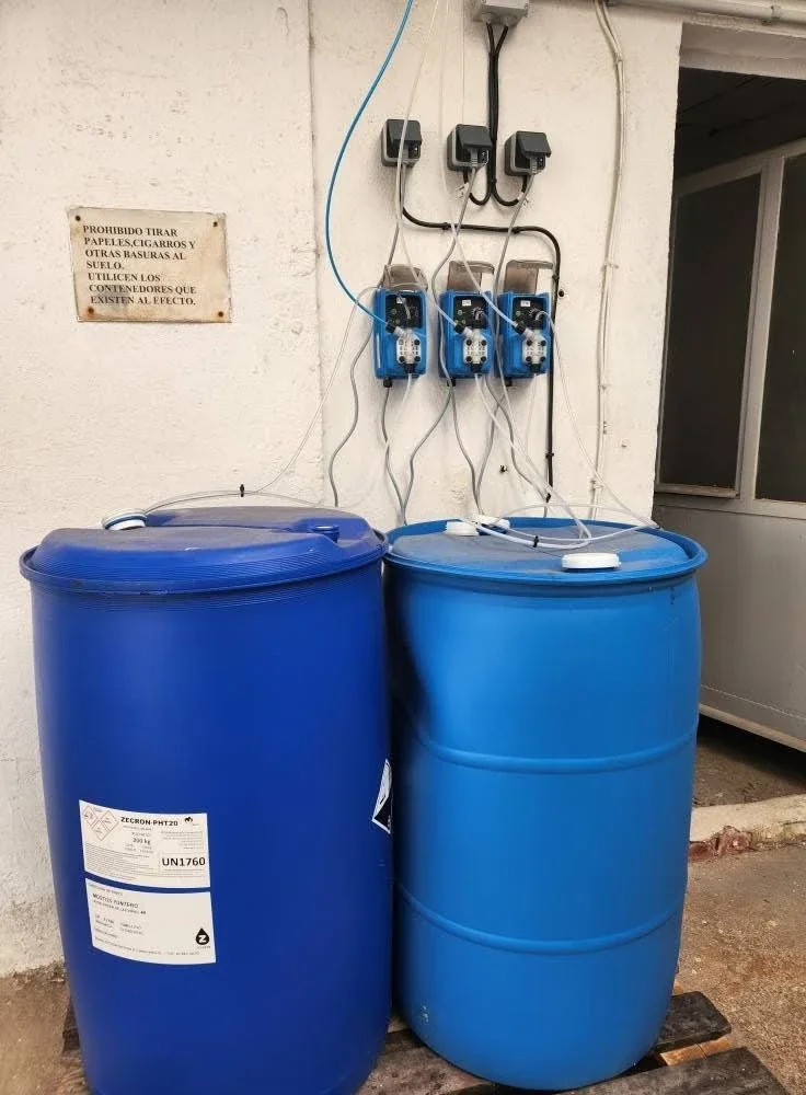Tres bombas dosificadoras en la pared conectadas a dos bidones azules de producto Zecron para el tratamiento del agua